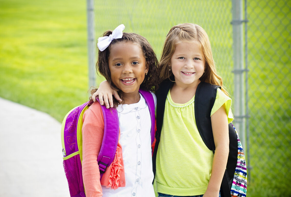 Two school age girls smiling with their arms on each other's shoulders