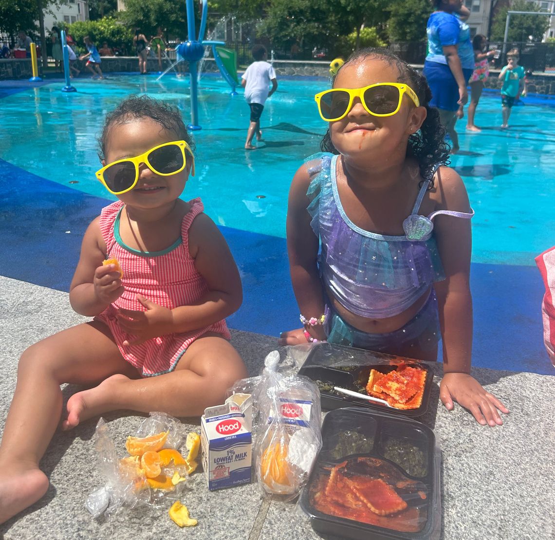 2 sisters smiling in sunglasses eating lunch by the pool