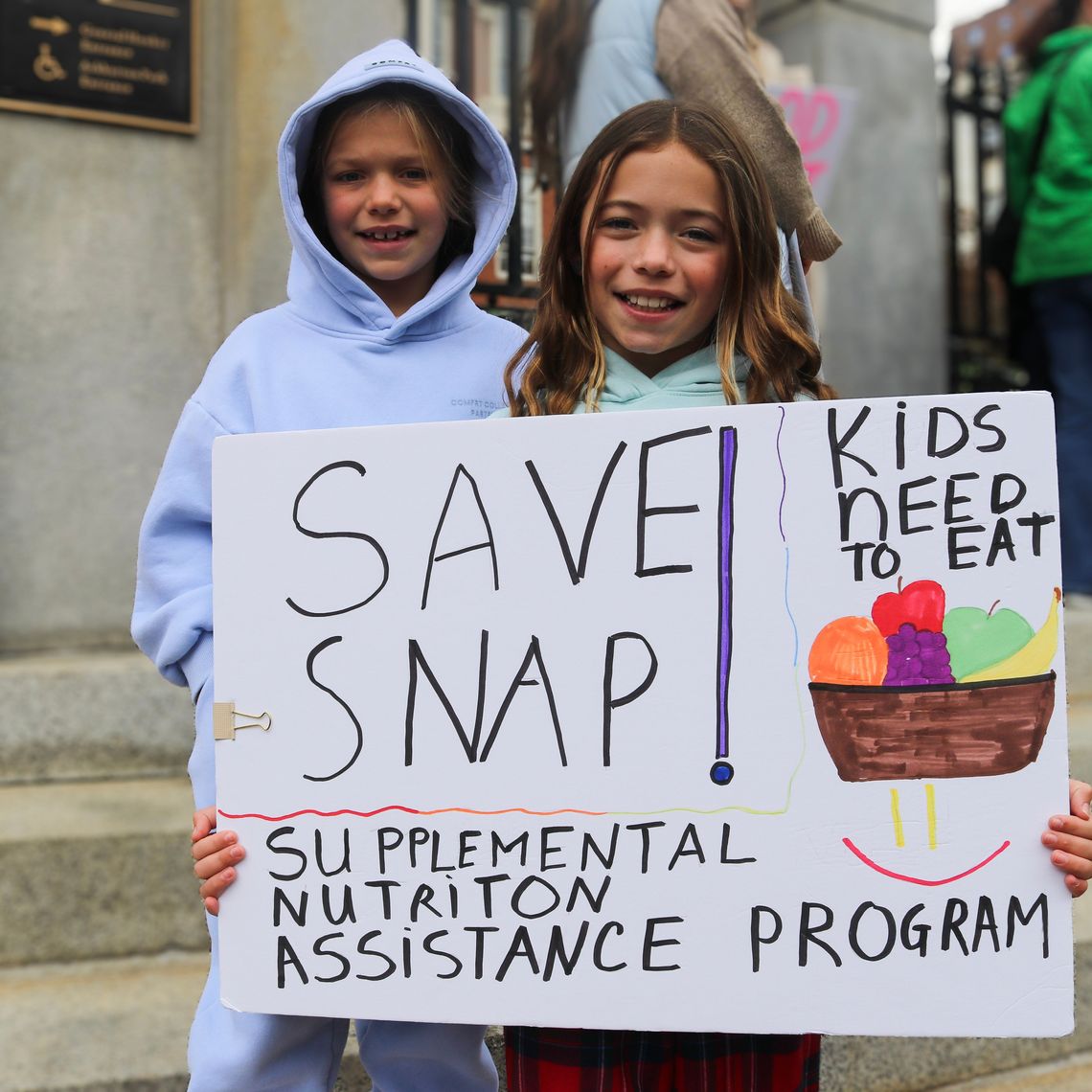 Two young girls hold a sign at the rally to fund SNAP