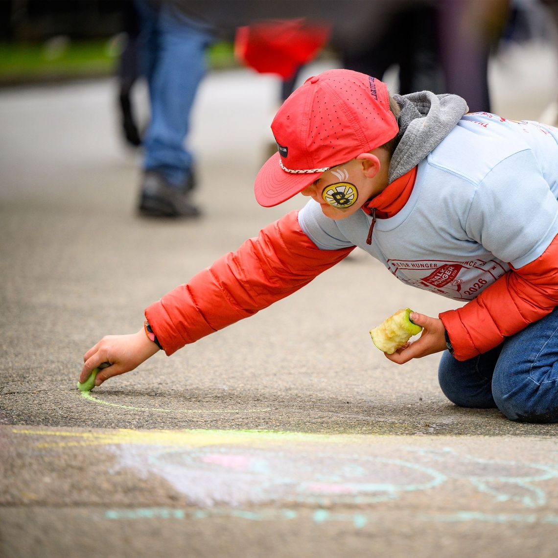 little boy holding an apple and drawing on the sidewalk with chalk