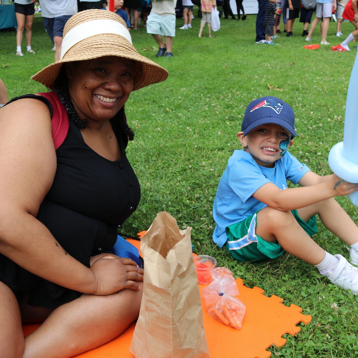 A parent and her child sit down in the shade at Waltham Summer Eats.